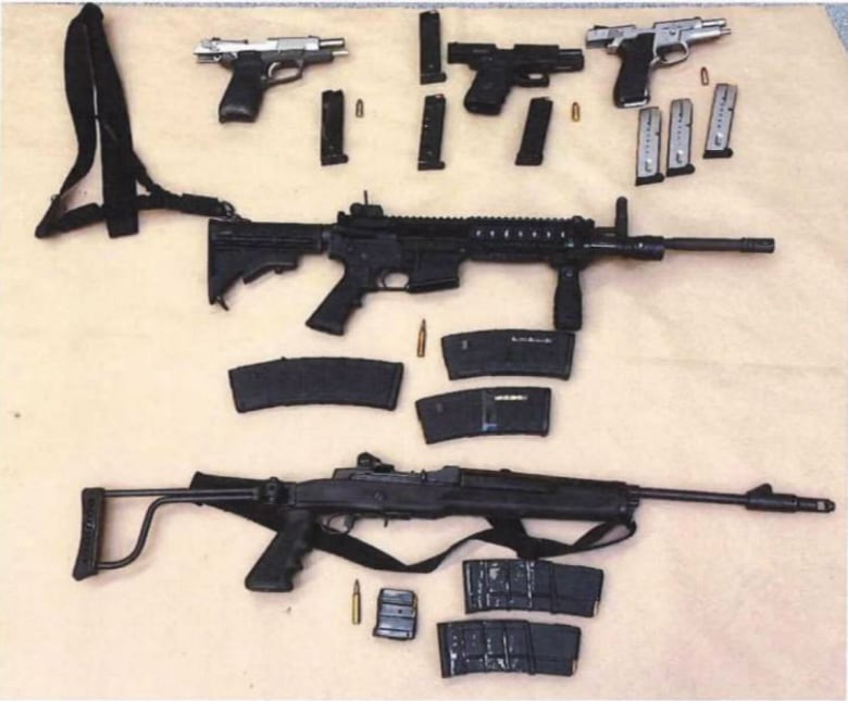 An arrangement of firearms including rifles and pistols are laid out on a beige background