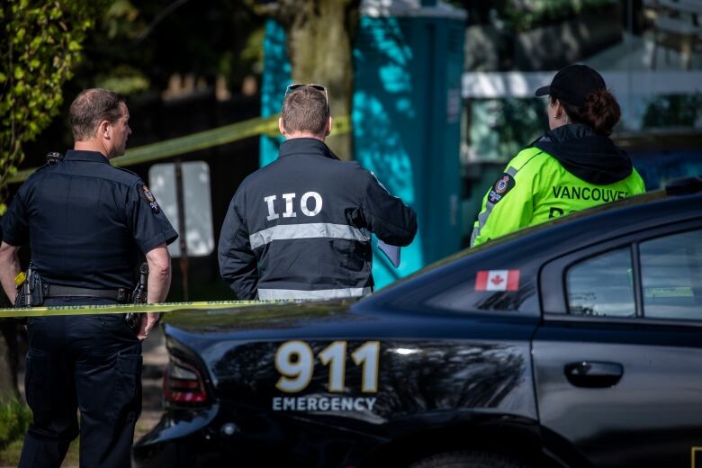 Vancouver police officers and detectives with the Independent Investigations Office stand together wearing branded jackets behind yellow police tape.