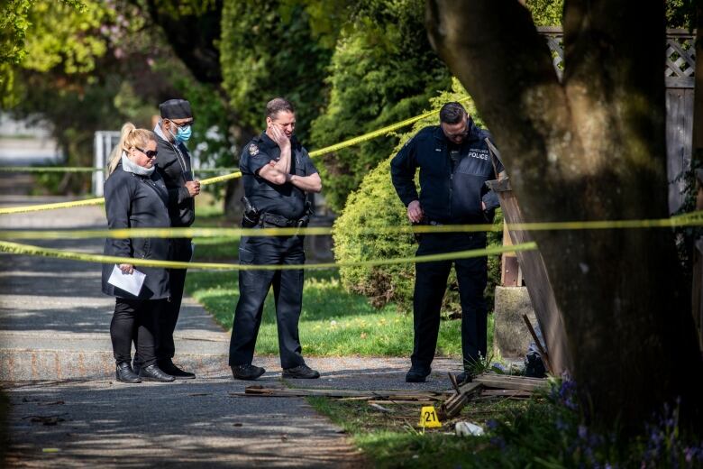 Vancouver police officers and detectives with the Independent Investigations Office stand together wearing branded jackets behind yellow police tape.