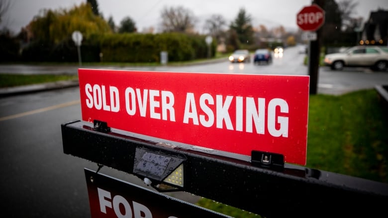 A red 'sold over asking' sign is pictured on a rainy day.