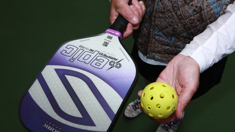 A woman holds a pickleball paddle and ball in this close-cropped photo.