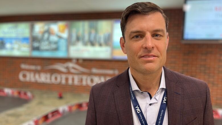 A man with short dark hair wearing a dark blazer over a white shirt and standing inside an airport lobby.