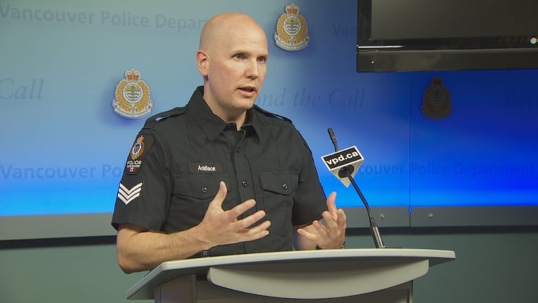 A bald white man wearing a police uniform gestures at a podium.