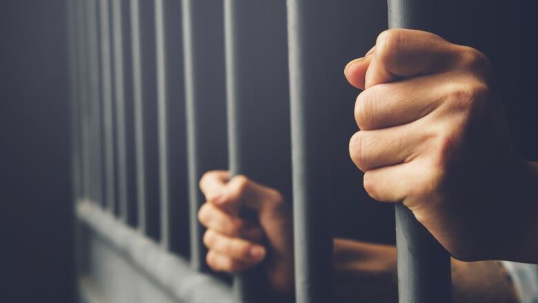 Two hands are seen holding jail bars.