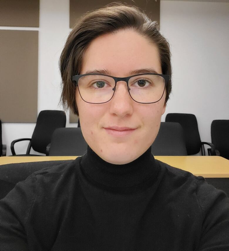 A person wearing glasses and a black turtleneck shirt looks at the camera.