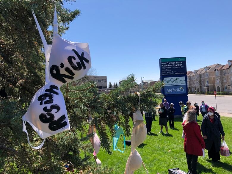 Bras hang from a tree, while women stand nearby