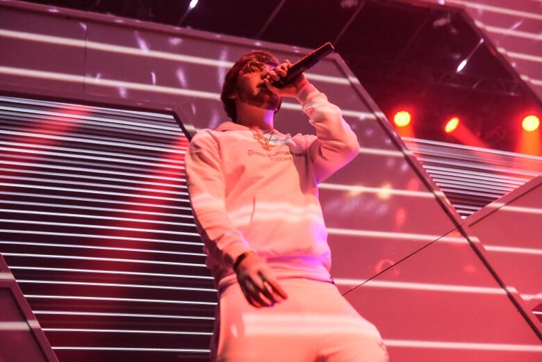 A person stands on a stage singing into a mic. They're coloured in reddish-pink light. 