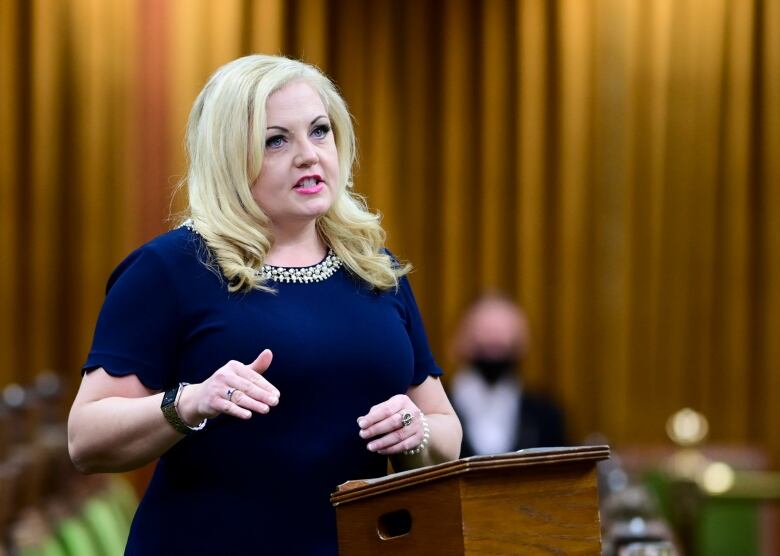 A woman in a blue dress motions with her hands as she speaks in the House of Commons.