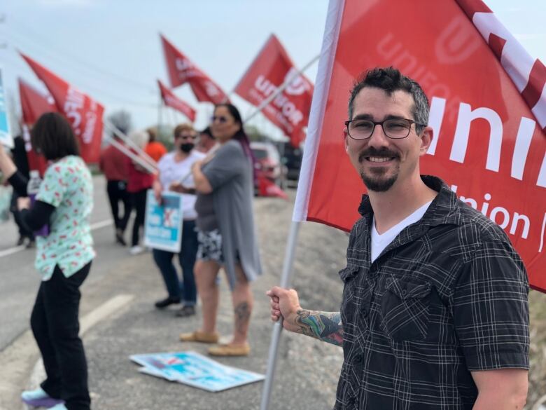 Man in a plaid shirt with a goatee, smiling, holds a red and white flag