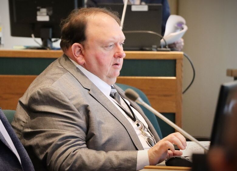 A man in a brown suit speaks into a microphone.