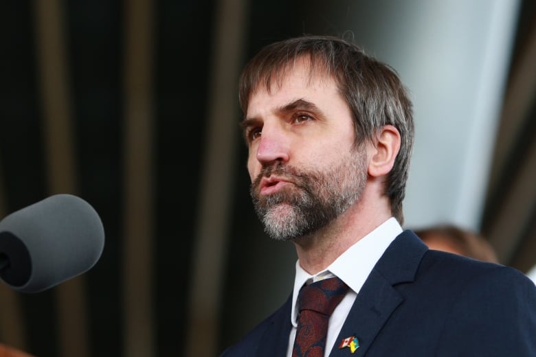 A man in a blue suit speaks at a podium. 