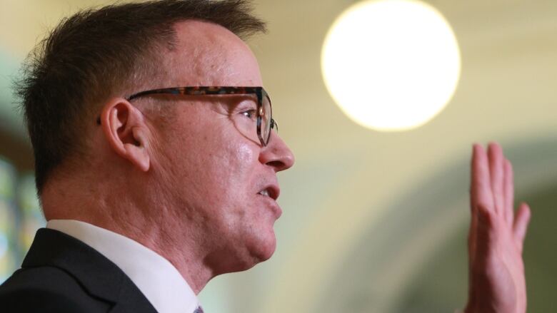 Kevin Falcon, a white man wearing glasses, gestures during a speech.