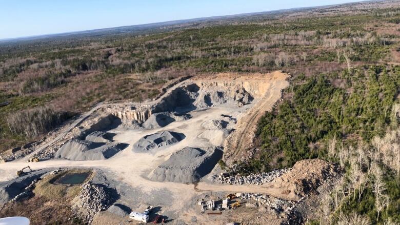 A view of a quarry from above. There are vehicles parked near where rock has been blasted. 