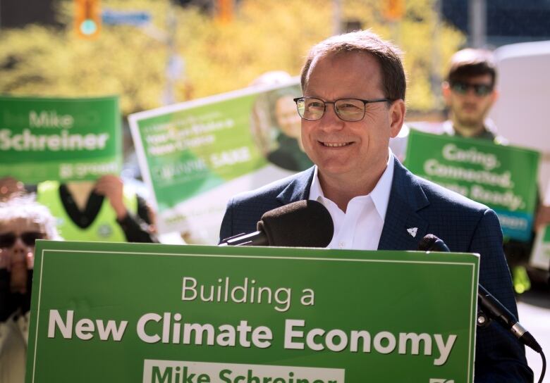 Man at podium with green and white signs behind him