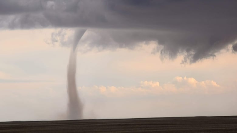 Dark clouds with a landspout tornado is seen on a farm field.