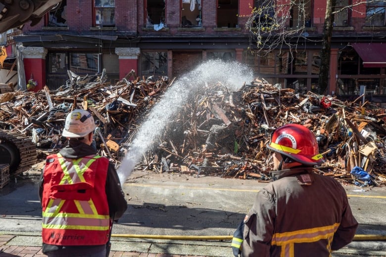 Two firefighters spray water onto the rubble where a building burned down.