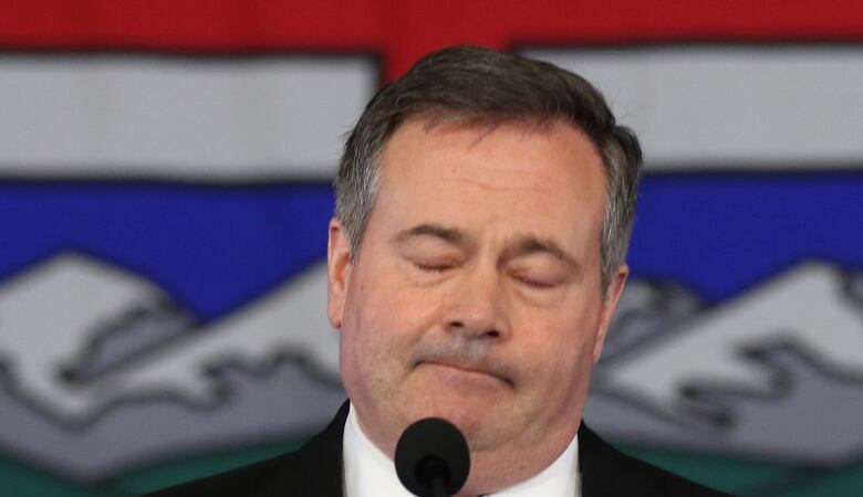 a politician closes his eyes, frowns and tilts his head, while pausing during a speech.