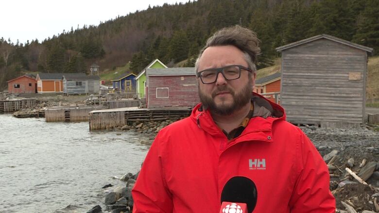 A man wearing a bright red jacket stands by a wharf.