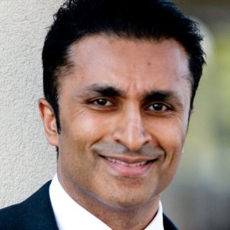 A man wearing a black suit and white shirt looks at the camera smiling. 