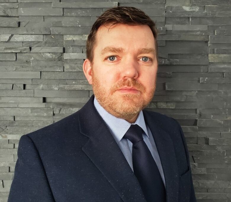 A man in a suit in front of a grey brick background