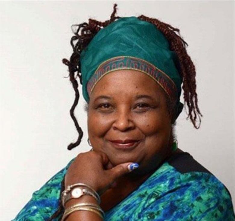 A Black woman with locs wearing a green headdress and top