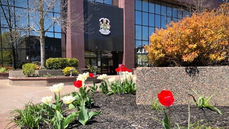 Red and white flowers shown in foreground in front of a red-brick-and-glass building labelled city hall.