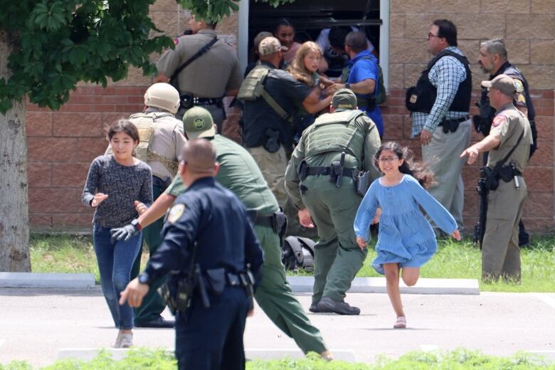 Frightened children flee a building, guided by police officers. 