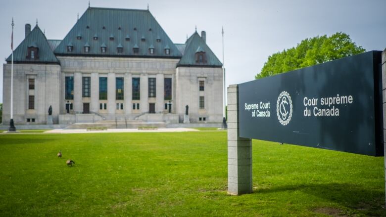 A large square building with a green roof. In the forefront of the image, a sign reading 'Supreme Court of Canada' is visible.