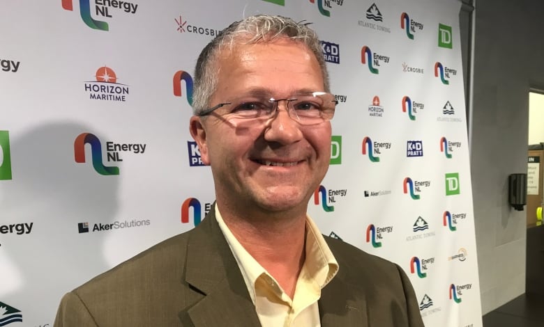 A man wearing a grey suit standing in front of a backdrop which reads Energy NL. 