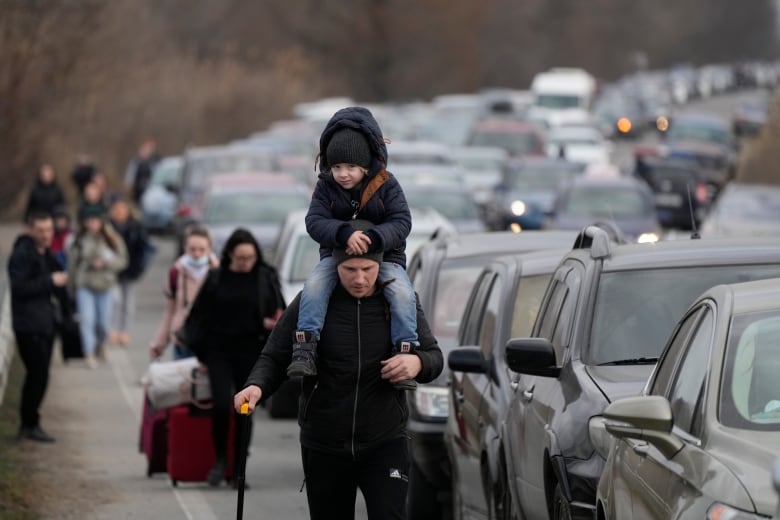 Refugees walk along vehicles.