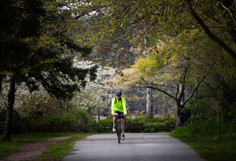 A man in a green high-visibility jacket rides a bicycle down a bike path.