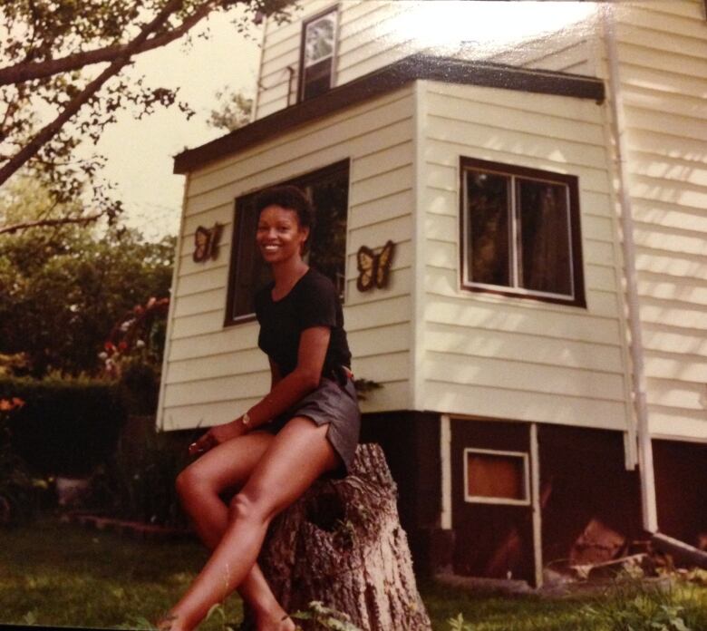 A Black woman with short hair leaning against a tree stub