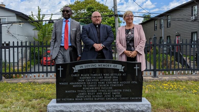 Three people standing behind a black gravestone