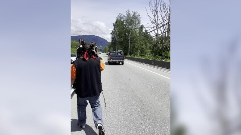 A man in an orange vest is seen looking at a blue pickup truck in the distance on a highway.