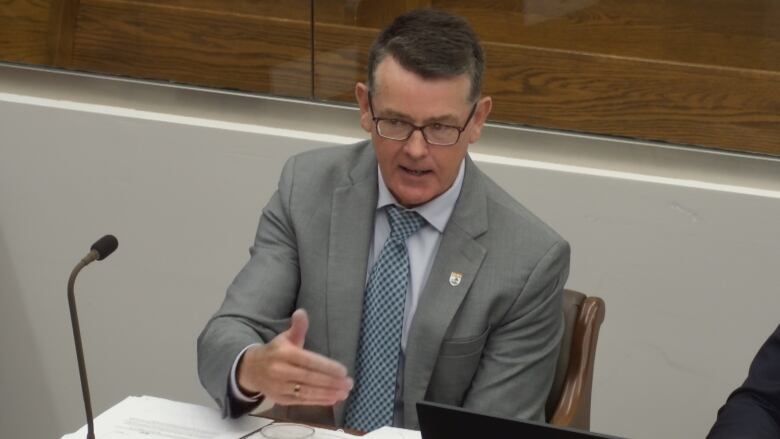 Man in glasses and wearing suit and tie speaks from a microphoned desk in the Prince Edward Island legislature. 