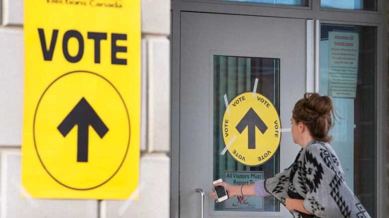 A woman reaches for a door with a yellow sign on it that says 