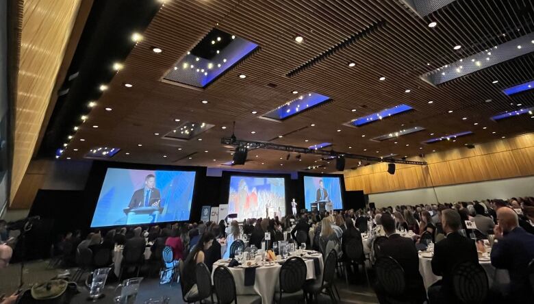 Large  projection screens and tables with people in the south hall of the convention centre.