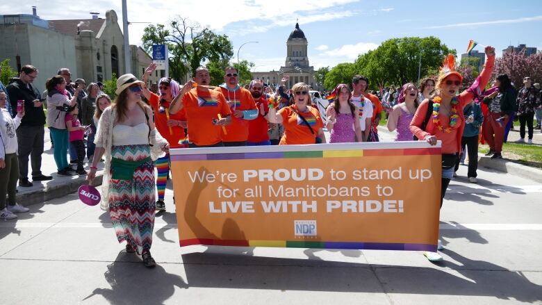 People march down a street during a Pride Parade carrying a sign that reads, 