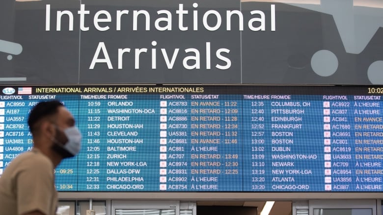 A man walks by the arrivals board in an airport.