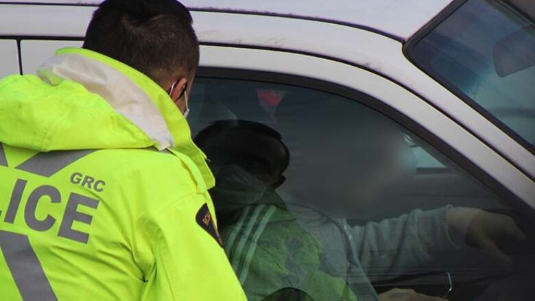 An RCMP officer in Burnaby looks through the window of a vehicle at a driver holding a device, which is prohibited in British Columbia.