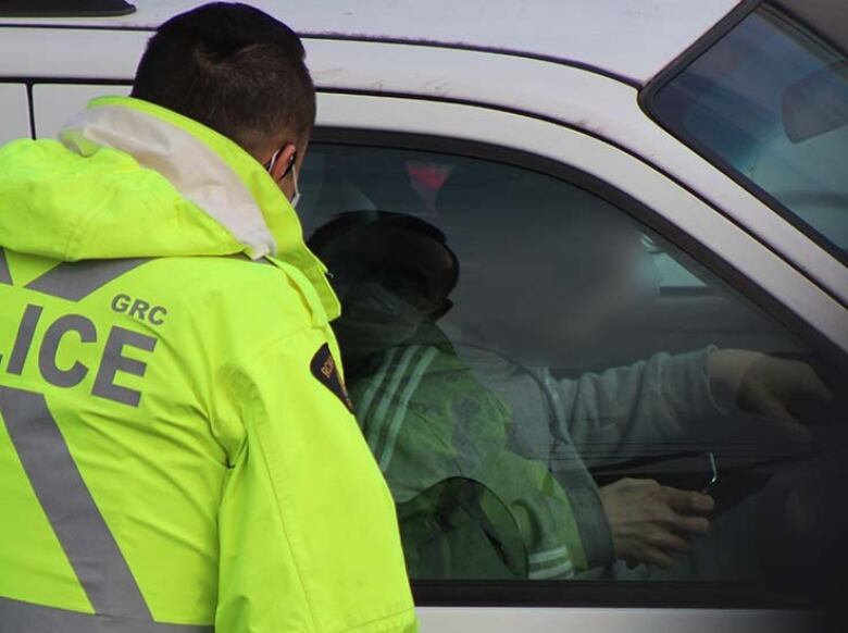 An RCMP officer in Burnaby looks through the window of a vehicle at a driver holding a device, which is prohibited in British Columbia.