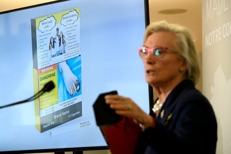 An example of cigarette packaging with expanded warnings, including a warning printed on the cigarettes themselves, is shown on a screen behind Minister of Mental Health and Addictions Carolyn Bennett as she participates in a news conference at the University of Ottawa Heart Institute in Ottawa, on Friday, June 10, 2022. 