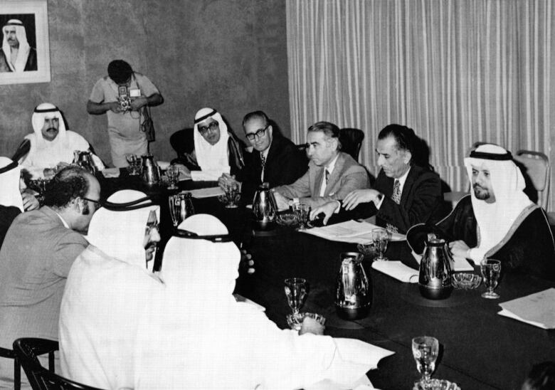 Arab oil ministers, some in suits others in white tradition head dresses, sit at a conference table.