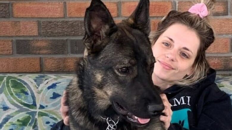 A woman in a pink ponytail holds a young black dog.