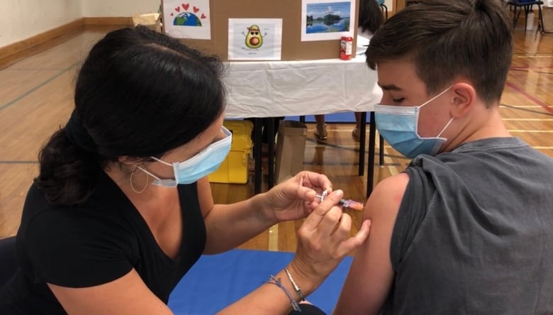 A woman gives a boy a needle in his arm.