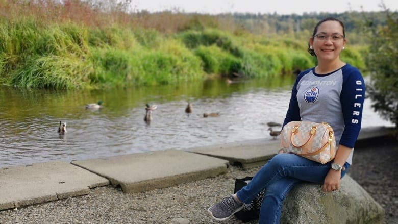 A Filipino woman wearing an Edmonton Oilers T-shirt poses near a river.