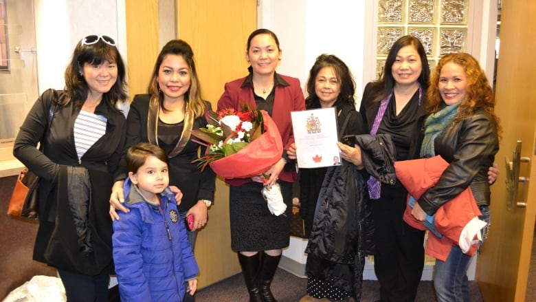 A group of Filipino women smile and pose for a photograph. One woman holds a bouquet of flowers.