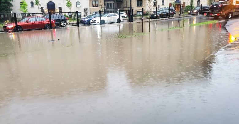 A huge puddle with a few cars up to their rims in water.