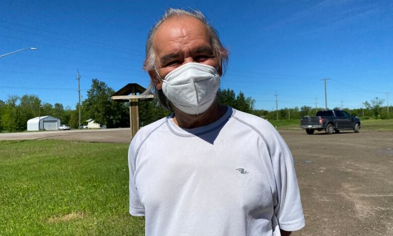 A man wearing a protective face mask stands in a yard, looking into the camera.