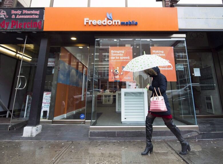 A women holds an umbrella as she walks past a Freedom Mobile store in Toronto on Thursday, November 24, 2016.